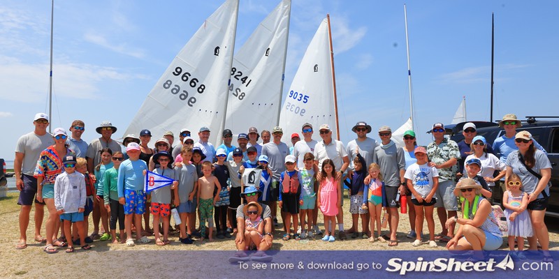 Sailors and families gathered ashore in front of Penguin sails at the 2026 Sweaty Penguin Regatta